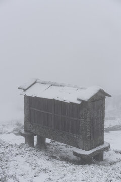 Espigueiro traditional structure for corn storage on a snow white winter landscape with snow falling in the north of Portugal