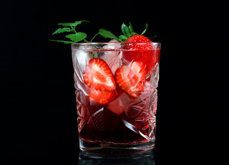 Red alcoholic drink with berry liquor, strawberry, ice cubes and mint in glass on black