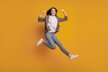 Fototapeta na wymiar Photo of cheerful lady raise biceps arm jump isolated on yellow background
