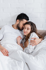 bearded muslim man hugging girlfriend with closed eyes in bed.