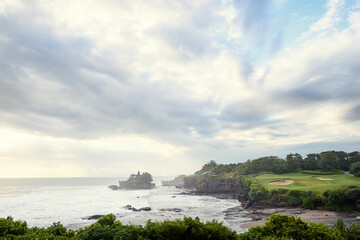 Fototapeta premium Beautiful balinese landscape. Ocean beach. Ancient hinduism temple Tanah lot on the rock against cloudy sky. Bali Island, Indonesia.