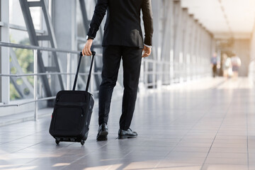 Cropped of businessman walking by airport with suitcase, back view