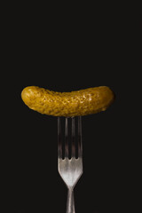 Crispy pickled cucumber on a fork, on a black background.