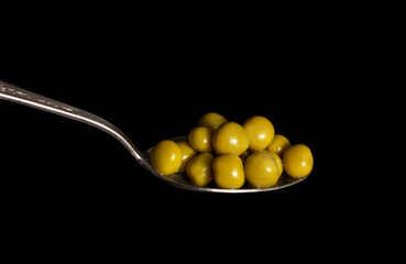 Pickled, green peas on a spoon, on a black background.
