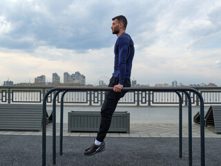 An athlete guy in a dark blue long sleeve is doing the uneven bars on the street.