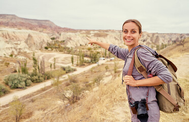 Fototapeta na wymiar Travel concept. Traveling young woman with backpack pointing away enjoying mountains view.