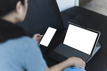 Woman sitting on the couch working online using mobile phone and laptop.