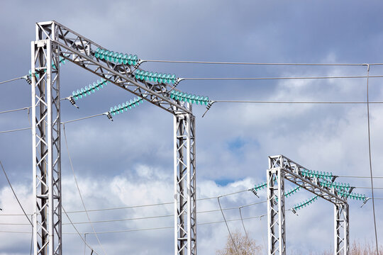 Two electric high voltage transmission H-frame power towers pylons single circuit three phases supported by insulators over cloudy stormy dark sky.