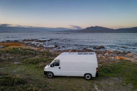 Camper van motorhome with solar panels drone aerial view on a sea landscape with mountains living van life in Galiza, Spain