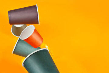 Disposable paper cups fall on an orange background. Glasses of different sizes and colors close up. Copy space and free space for text near the dishes.