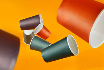 Disposable paper cups fall on an orange background. Glasses of different sizes and colors close up.