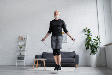 bearded man in sportswear exercising with jumping rope in modern living room. - Powered by Adobe