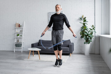 tattooed man in sportswear exercising with jumping rope in living room.