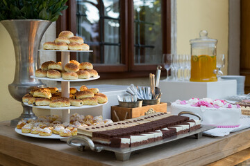 Close up of table with selection of cakes placed outdoors in front of a building on sunny summer afternoon