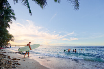 Hobby and vacation. Young man with surfboard on beautiful tropical beach.