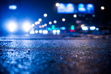 Rainy night in the big city, glare from the headlights of the parked car and a passing near the...