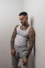 Obraz premium Retrato de un joven apuesto varón español tatuado posando apoyado en una pared blanca