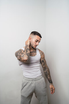 Retrato de un joven apuesto varón español tatuado posando apoyado en una pared blanca