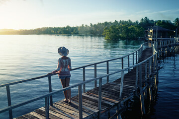 Vacation on tropical island.  Back view of young woman in hat enjoying sunset sea view from wooden bridge terrace, Siargao Philippines