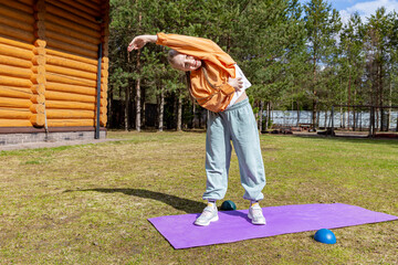 A teenage girl goes in for sports in the backyard, on a summer day, exercises while standing on a...