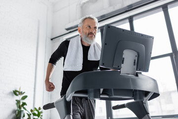 bearded man with towel running on treadmill at home.