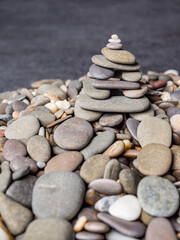 Fototapeta na wymiar Multi-colored oval pebbles one on top of the other make up a group. Sea pebble pyramid. Pebble mini-house. Stack of pebbles for spa, balance, meditation and zen themes. Pebble background and texture