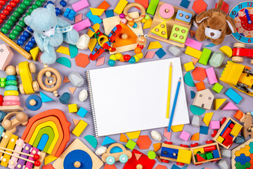Colorful educational wooden plastic and fluffy baby kids toys and blank notebook with colored pencils on gray background. Top view