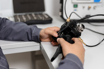 Tools for verifying the calibration and performance of the metrology laboratory. A man performs a hand-held pressure test. Connected hoses.