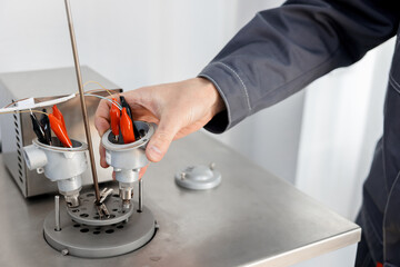 Thermocouple calibration in progress. A man tests temperature sensors in a metrology laboratory under reference conditions. Connecting wires to temperature sensors. - obrazy, fototapety, plakaty