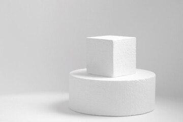 Two white geometric objects made of polystyrene: circle, square, standing one on top of the other on light monochrome background. Concept of an empty 3d podium for presentation of cosmetic products