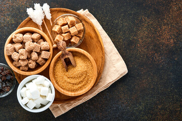 White sugar, cane sugar cubes, caramel in bamboo bowl on dark brown table concrete background. Assorted different types of sugar. Top view or flat lay.
