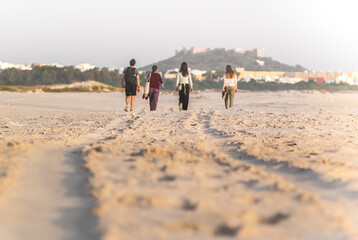Friends walk on the beach on a sunny day. Back view. Castle and old town in the background.