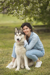 Beautiful brunette girl sitting on the grass with her funny friend malamute dog