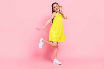 Fototapeta na wymiar Full length photo of funky charming school girl wear yellow dress dark eyewear smiling dancing isolated pink color background