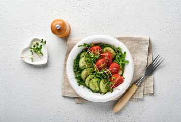 Fresh salad with tomato, cucumber, vegetables, microgreen radishes in white plate on grey stone background. View from above. Concept vegan and healthy eating.