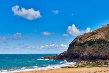 Fototapeta premium Image of the East section of Geve le Lecq, Jersey CI with sand, rocks, headland and choppy sea in the sunshine with some cloud