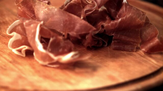 Super slow motion on the cutting board falls pieces of Spanish ham. Filmed on a high-speed camera at 1000 fps.On a wooden background. High quality FullHD footage
