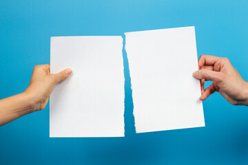 Kid and woman hands holding pieces of torn white paper sheet on light blue background