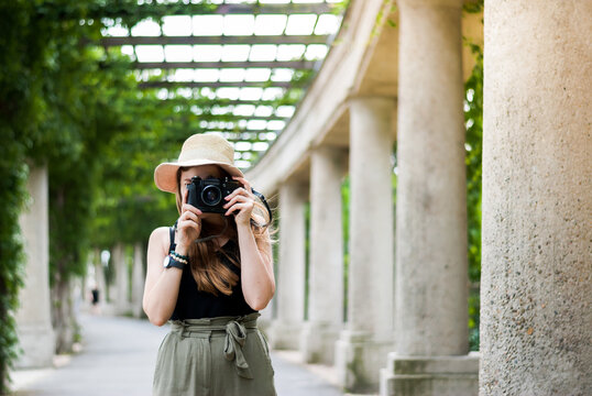 Girl travel photographer in a hat takes a photo of an old vintage camera.  Columns arch on background.
