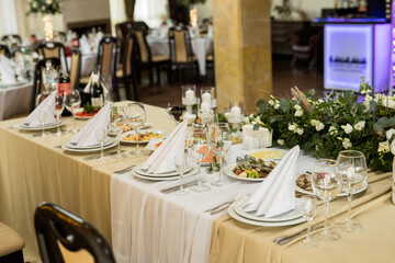 Close up of festive table setting with wine glasses, fresh flowers on beige tablecloth