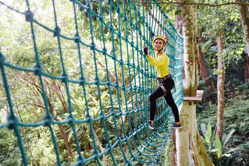 Young woman with climbing gear in an adventure extreme park climbing or passing on the rope road.