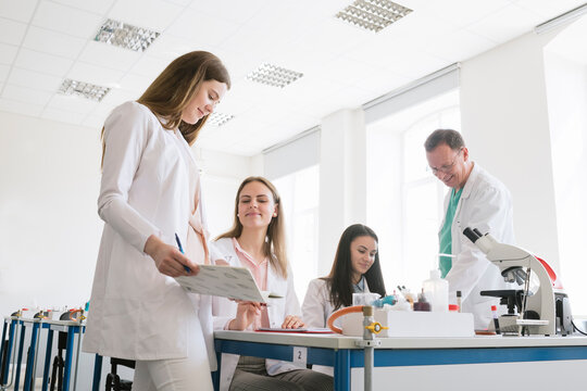 Students And Teacher In White Coats Discussing In Science Class