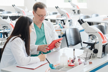 Scientists in white coats using tablet in lab