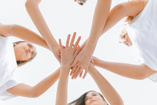 Young female friends with stacked hands against sky