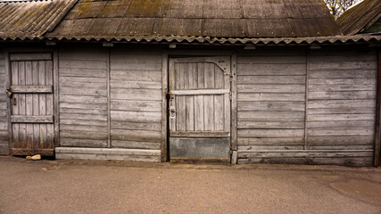 Fototapeta na wymiar Grye mooden rural buildings. Old sheds. Zoo storage rooms. The doors are locked