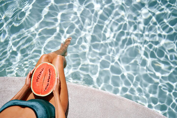 Concept of diet, spa and cosmetics. Enjoying tropical fruits, suntan and vacation. Young slim woman in green swimsuit sitting near swimming pool holding watermelon.