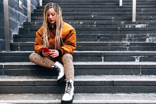 Young woman wearing jacket using mobile phone while sitting on steps