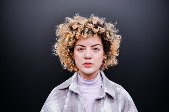 Beautiful curly haired woman against black wall