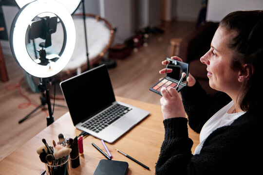 Smiling woman holding Make-up Palette while recording make-up tutorial at home