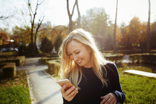 Blond woman laughing while suing smart phone in park